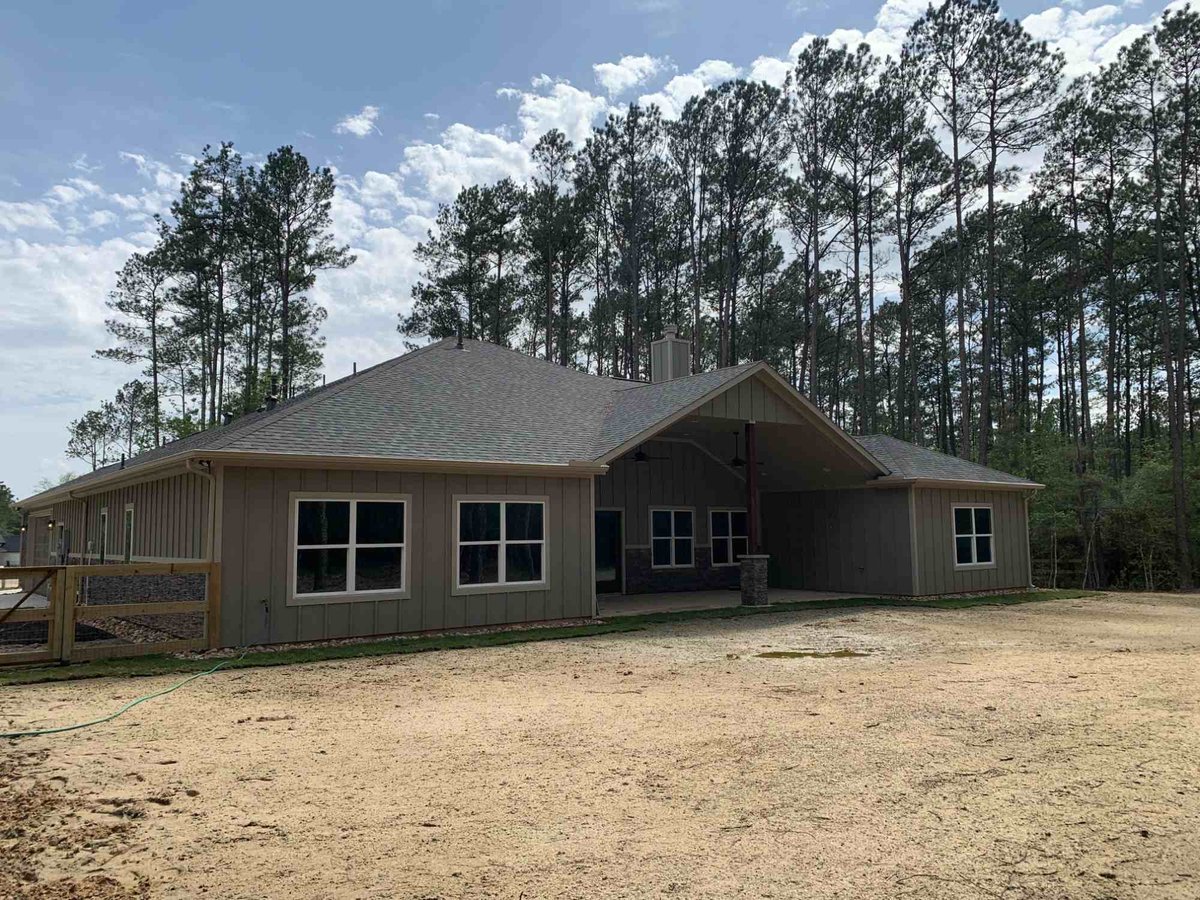 Rear exterior of a residential new construction home by Wonderview Home Services surrounded by pine trees in Magnolia, TX.