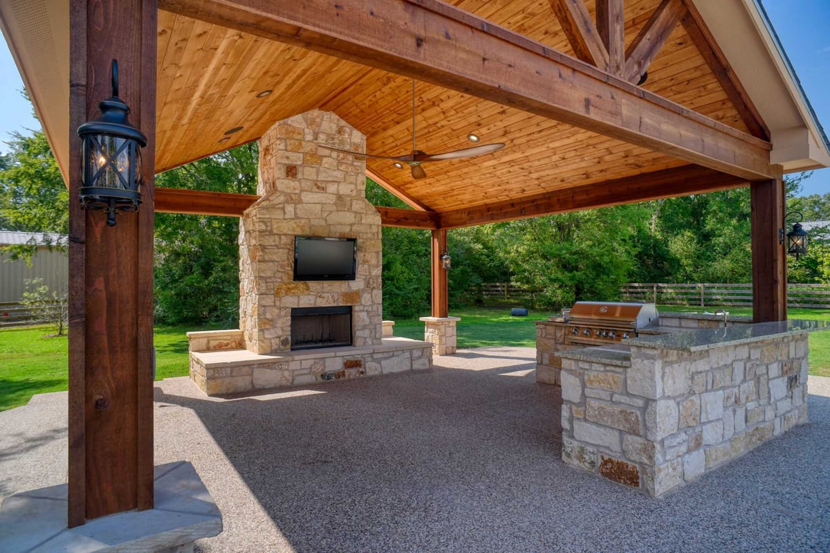 Outdoor kitchen and fireplace under a timber frame patio by Wonderview Home Services in Montgomery, TX.-optimized
