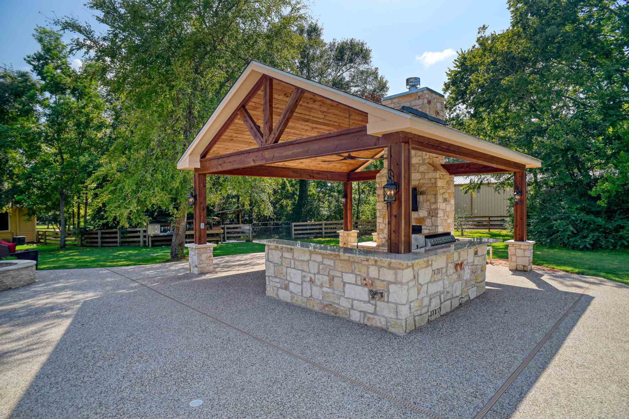 Outdoor living pavilion with fire pit and stone kitchen by Wonderview Home Services in Montgomery, TX.