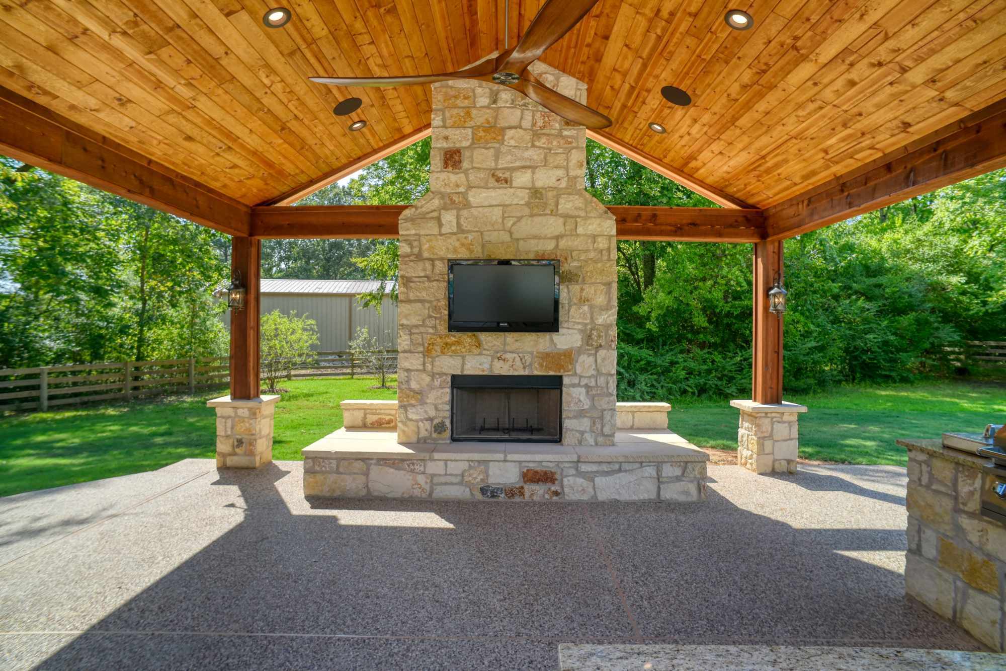 Stone fireplace with mounted TV beneath a cedar patio pavilion by Wonderview Home Services in Montgomery, TX.-optimized